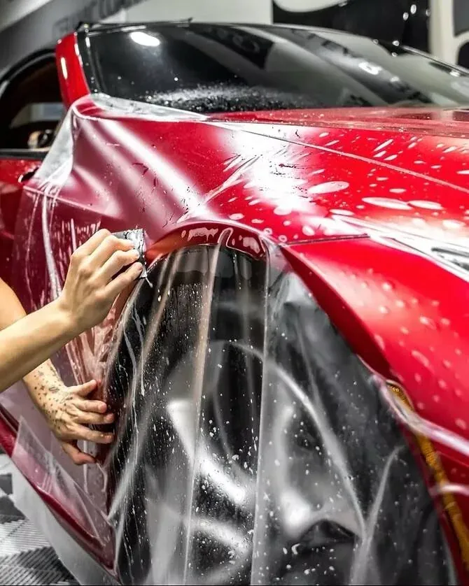 Clear paint protection film being squeegeed onto a red car's front fender