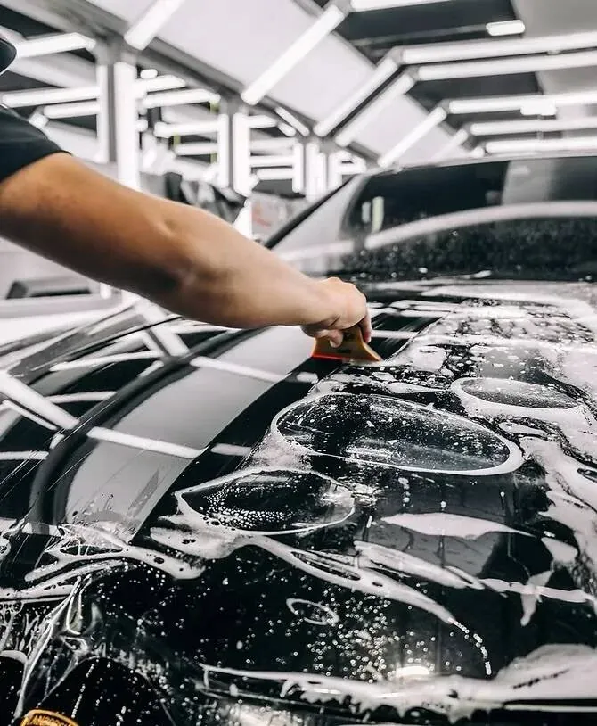 Clear bra film being laid onto a black car's hood with slip solution